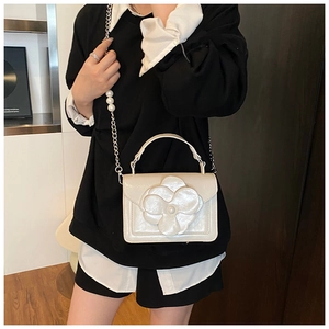 Detailed view of cream crossbody bag featuring 3D flower and pearl chain strap on model