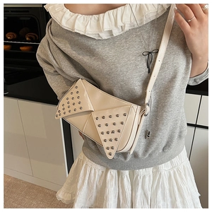 Sac bandoulière beige en similicuir avec rivets argentés dans une scène de vie