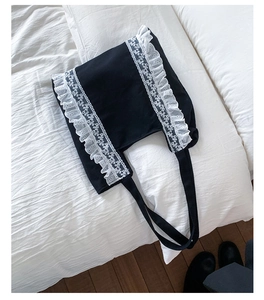 Close-up of black canvas tote bag with intricate white lace embroidery on textured fabric