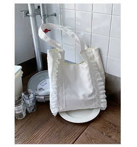 Detail of white canvas tote bag featuring ruffled edges and delicate lace embroidery accents