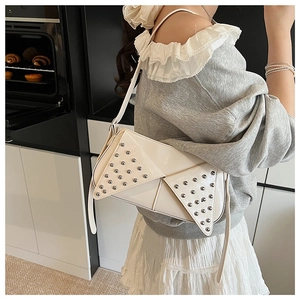 Détail d'un sac à bandoulière blanc à rivets porté par un mannequin dans un cadre moderne