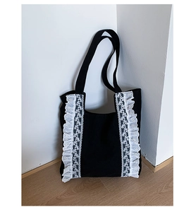 Detail of black canvas tote bag featuring white ruffled lace trim and wide shoulder straps
