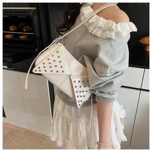 Détail d'un sac à bandoulière blanc brillant avec clous argentés dans une cuisine moderne