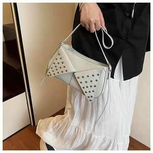 Detail of a chic cream crossbody bag with metal rivets worn by a model in a stairwell