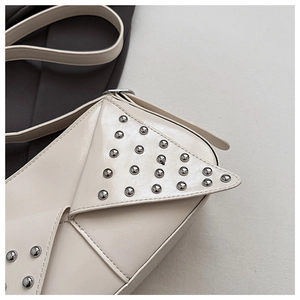 Gros plan du sac en cuir crème avec rabat géométrique et rivets métalliques argentés