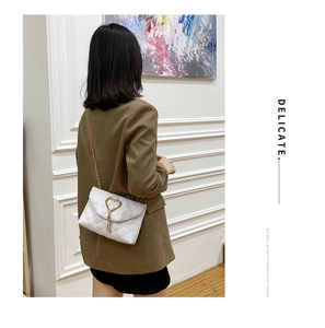 Detail of white quilted crossbody bag with gold heart clasp worn over a brown blazer