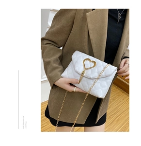 Detail of white quilted crossbody bag featuring a gold heart lock and fringe tassel