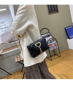 Detail of black quilted crossbody bag with gold heart clasp and tassel chain strap