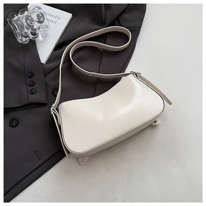 Gros plan d'un sac carré blanc crème à rivets sur un blazer gris et accessoires