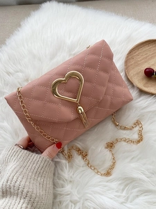 Pink quilted heart crossbody bag with gold chain strap on soft plush background