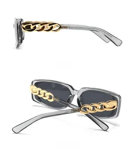 Detail view of modern sunglasses featuring chunky gold chain temples and grey frames