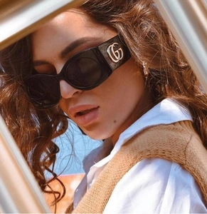 Detail of wide-frame black sunglasses with golden double G logo on thick temples