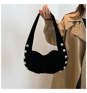 Detail shot of silver spherical rivets on a black velvet hobo bag held by a model