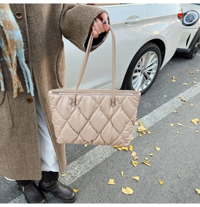 Detail view of beige quilted puffer tote bag with silver zipper and long shoulder straps