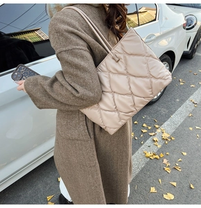Detailed view of beige quilted tote bag with diamond pattern on woman's shoulder in autumn