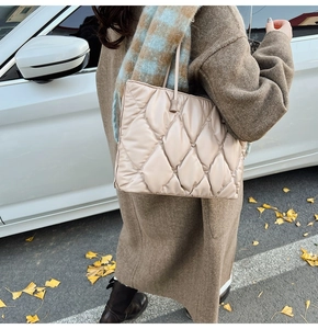 Detail of beige quilted tote bag showing rhombus texture and slim handles in autumn street
