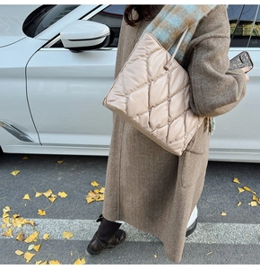 Detailed view of quilted beige puffer tote bag styled with a warm autumn coat outdoors