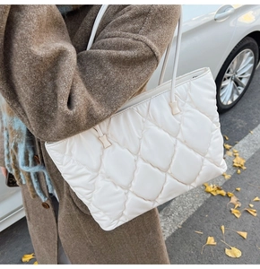 Close-up of white quilted tote bag worn with a brown coat in an autumn street setting