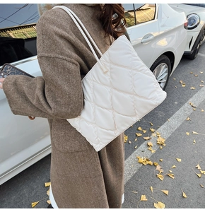 Close-up of a white quilted tote bag worn over a brown wool coat in an urban street setting