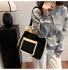 Detail of a large black suede tote bag with white faux shearling trim worn by a model