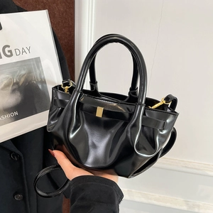 Detail view of black glossy pleated handbag with gold buckle and adjustable shoulder strap