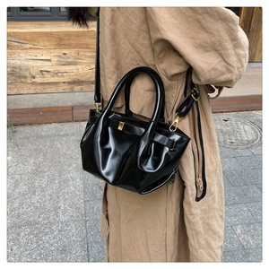 Detail of glossy pleated black bucket bag with gold buckle and adjustable shoulder strap