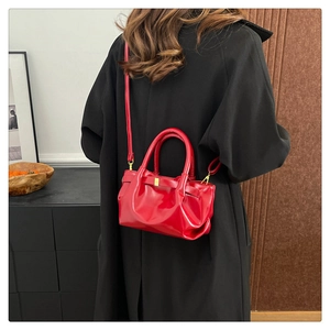 Red glossy pleated crossbody bag with gold hardware shown on a model for size perspective