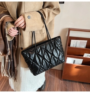 Close-up of black quilted leather tote bag with elegant pleated stitching and slim straps