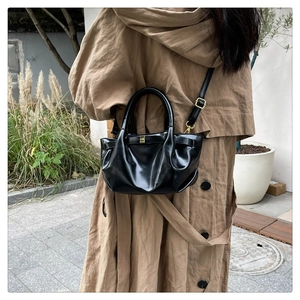 Outdoor lifestyle shot of a black pleated dumpling bag worn with a beige trench coat