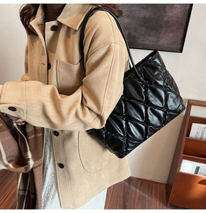 Close-up of a black quilted tote bag with a glossy texture on a wooden background