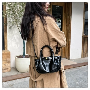 Detail of black glossy pleated dumpling bag with golden hardware and cylindrical handle
