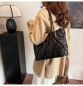 Detail of black glossy quilted tote bag with elegant diamond pattern and thin shoulder straps