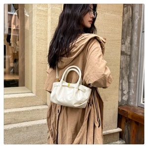 Chic cream glossy dumpling bag with gold rings shown in a stylish street fashion setting