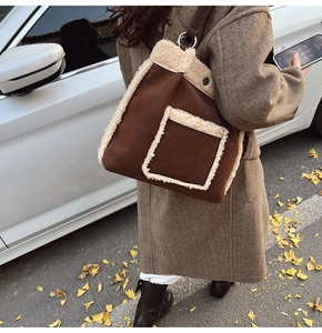 Brown suede tote bag with white fleece trim and leather straps on an autumn street background