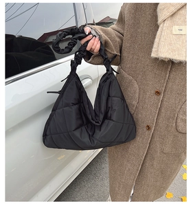 Detail of black quilted tote bag with elastic ruched handle in outdoor street setting