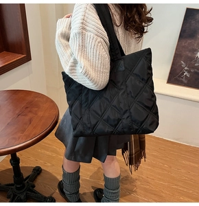 Detail of black quilted nylon tote bag showing diamond stitch pattern and wide strap