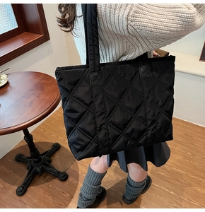 Borsa tote in nylon nero trapuntato indossata da una modella in un caffè accogliente