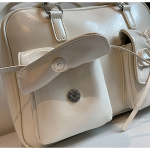 Detailed close-up of the magnetic silver buckle and stitching on a cream shoulder bag