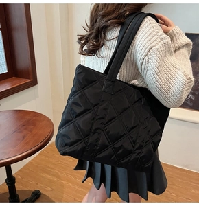 Detailed view of black quilted nylon tote bag with rhombus embroidery on a shoulder