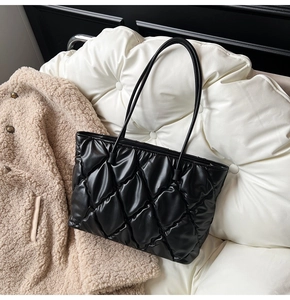 Close-up of black quilted puffy tote bag with glossy finish and cylindrical handles