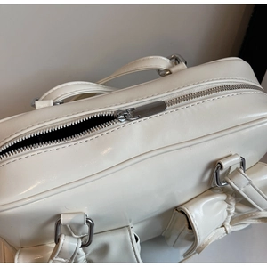 Close-up of the smooth silver metal zipper on a white synthetic leather shoulder bag