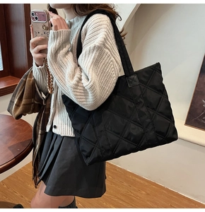 Detailed view of a black quilted nylon tote bag with rhombus embroidery on a model