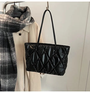 Quilted black tote bag with ruffled texture hanging over a winter trench coat