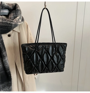 Close-up of black quilted tote bag with diamond lattice pattern and slender shoulder strap