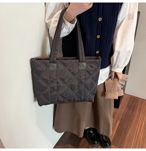 Dark brown quilted nylon tote bag worn by a model in a stylish urban commuter outfit