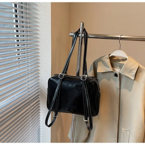 Detail of glossy black shoulder bag featuring contrast white stitching and silver buckles