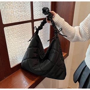 Detail of black quilted nylon bag featuring a bow shoulder strap and diamond stitching