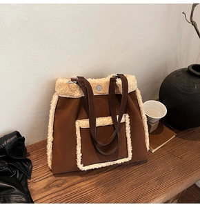 Detail of suede tote bag featuring sherpa trim and leather straps on a wooden table