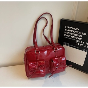Close-up of red patent leather shoulder bag with bow details and white contrast stitching
