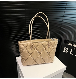 Detail of beige quilted tote bag showing padded nylon texture on white pedestal